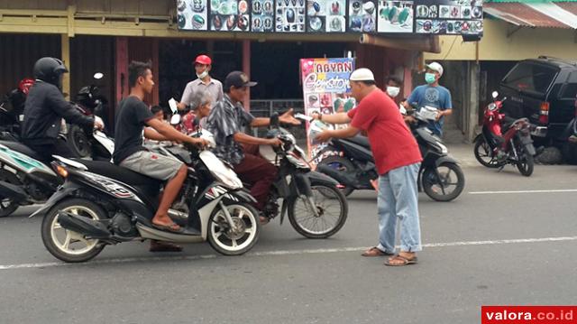 Pemilik Abyan Gemstone, Ronal (baju merah) membagikan masker pada pengendara yang lewat di depan warungnya, di Jl Alai-Bypass, Jumat (23/10/2015) siang. (istimewa)