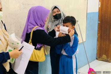 Siswa sebuah sekolah dipasangkan masker yang benar oleh gurunya. (humas)