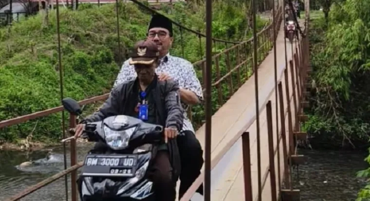 Anggota Fraksi Partai Golkar DPR RI Dapil Sumbar II, Benny Utama diboncengi warga dengan sepeda motor, melewati jembatan rajang, saat reses perorangan masa persidangan IV Tahun 2024-2025 di daerah terluar dan terdepan di Kabupaten Pasaman. (istimewa)