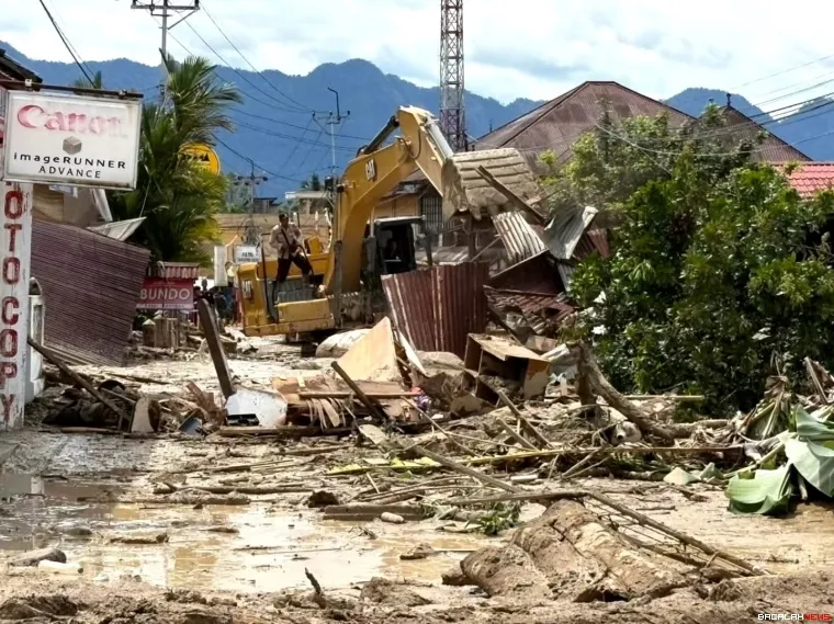 Petugas terlihat membersihkan material kayu dengan alat berat 